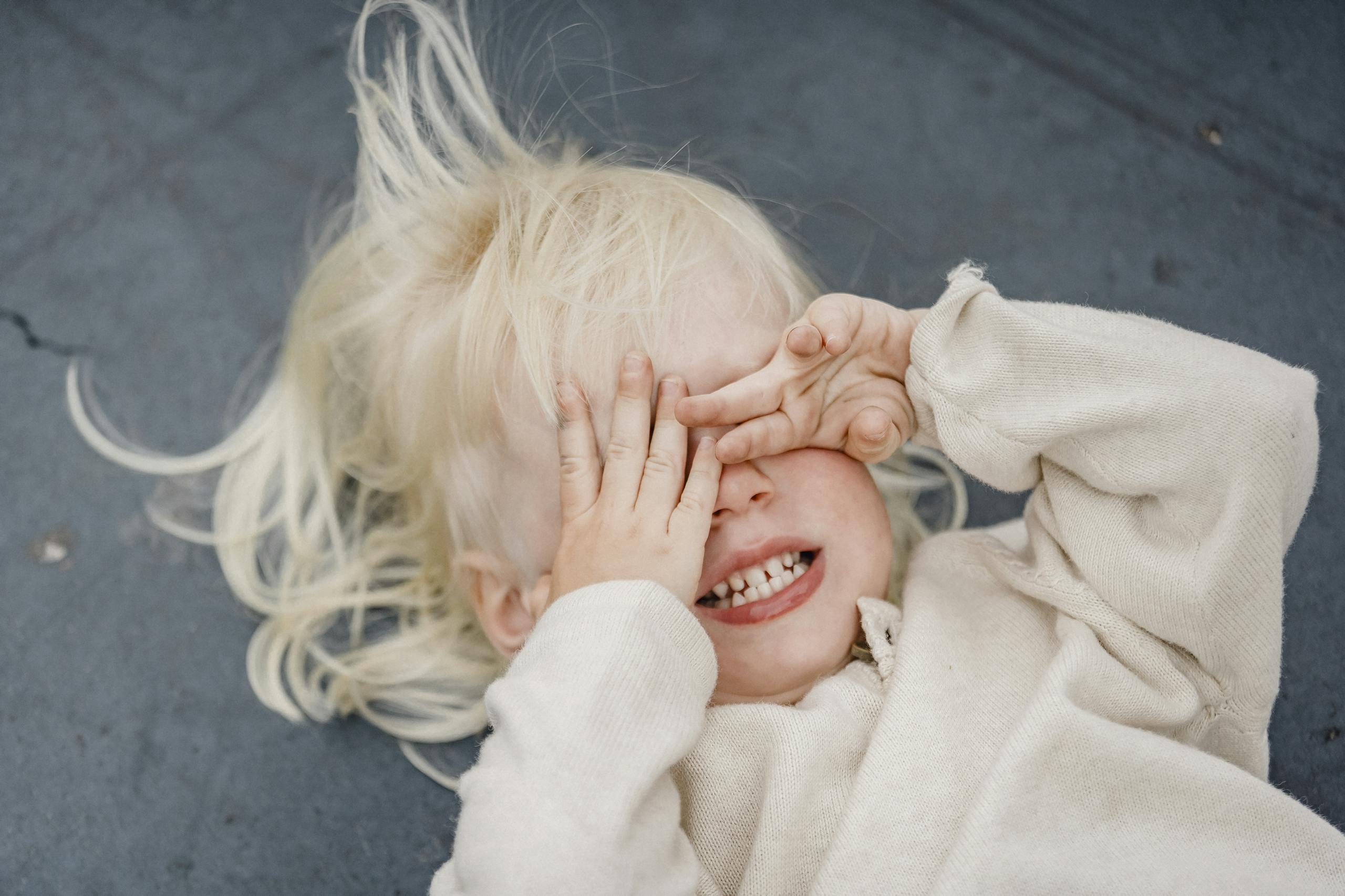 Cute blond child lying down with hands covering eyes, showcasing innocence and playfulness.